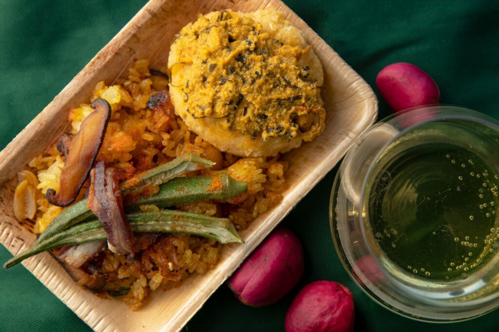 A rectangular plate with rice and okra. A glass of wine sits next to it. 