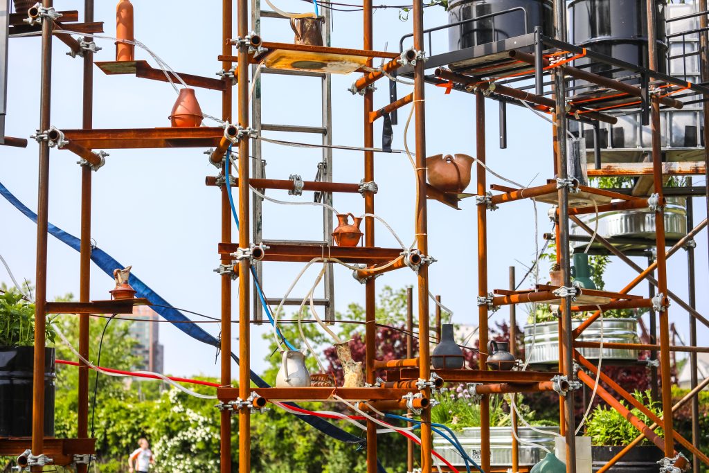 Copper-colored scaffolding holds up pots and tubs, with clear tubes bringing water to each of them.